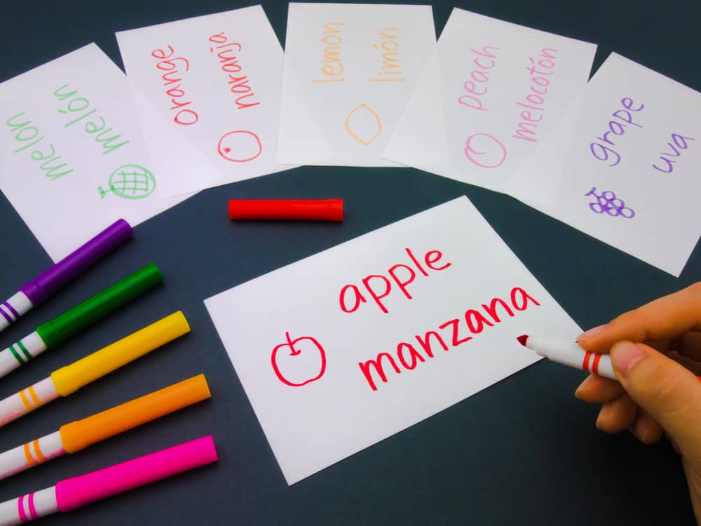 Imagen de una mano escribiendo en una tarjeta de vocabulario, con otras tarjetas ya preparadas con palabras en inglés y español.