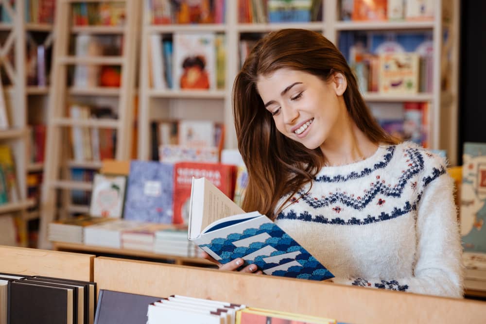 Una joven sonriente lee un libro en una librería. Imagen perfecta para artículos sobre cómo elegir el libro ideal para aprender inglés.