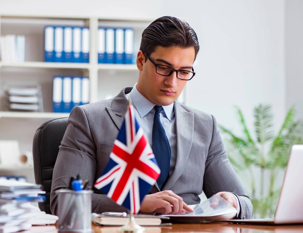 Hombre de negocios trabajando en un escritorio con una bandera del Reino Unido, representando la etiqueta empresarial británica.