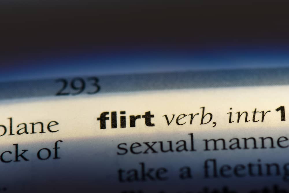 Primer plano de una página de diccionario que muestra la definición de la palabra inglesa "flirt" (coquetear), destacando su significado como verbo intransitivo.