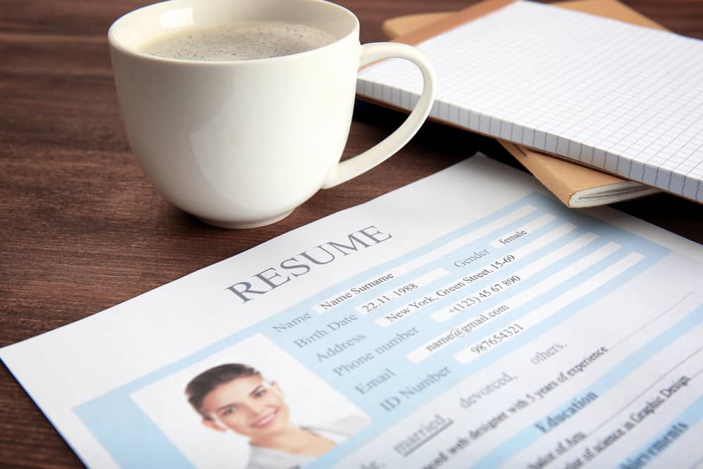 Un currículum vitae en inglés o resume con una taza de café y una libreta sobre una mesa de madera.