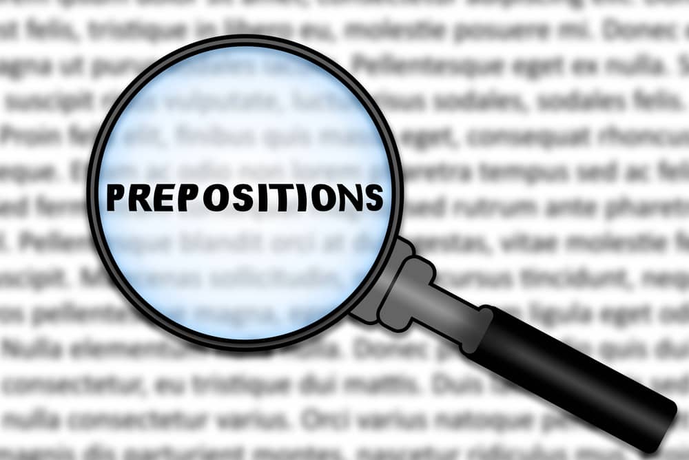 Lupa enfocando la palabra "Prepositions" sobre un texto borroso. Concepto de preposiciones en inglés.